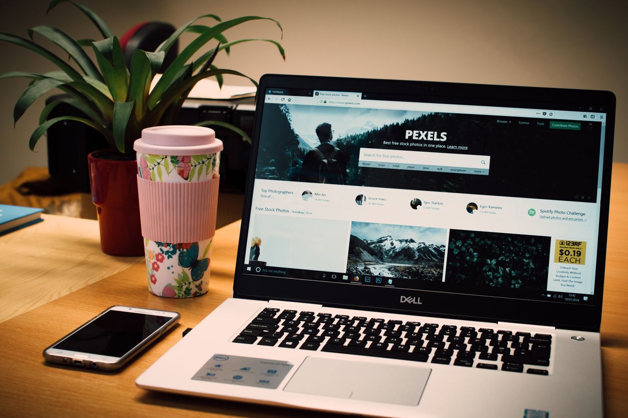 Un espace de bureau soigné avec un ordinateur portable affichant un site de photos de stock et un smartphone.