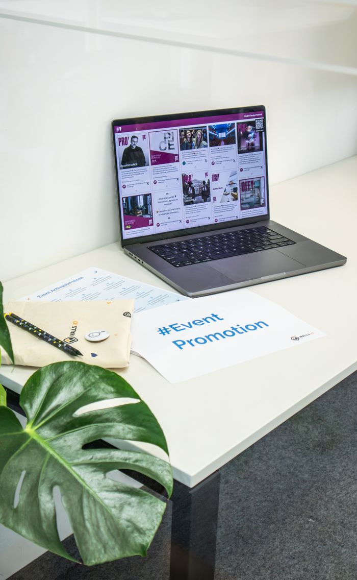 A tidy office setting with a laptop showing social media, along with papers and a plant, used for event promotion.